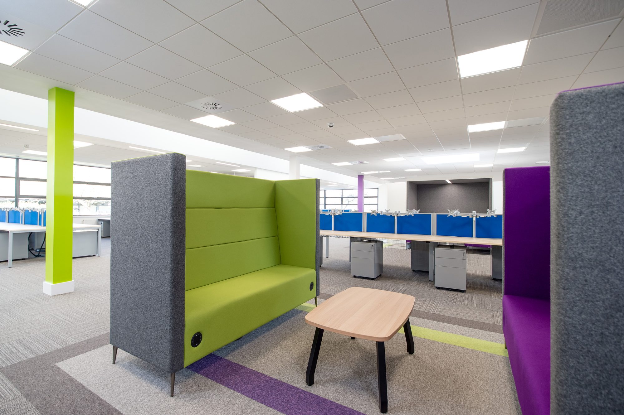 Green high-back acoustic sofa near desk benches