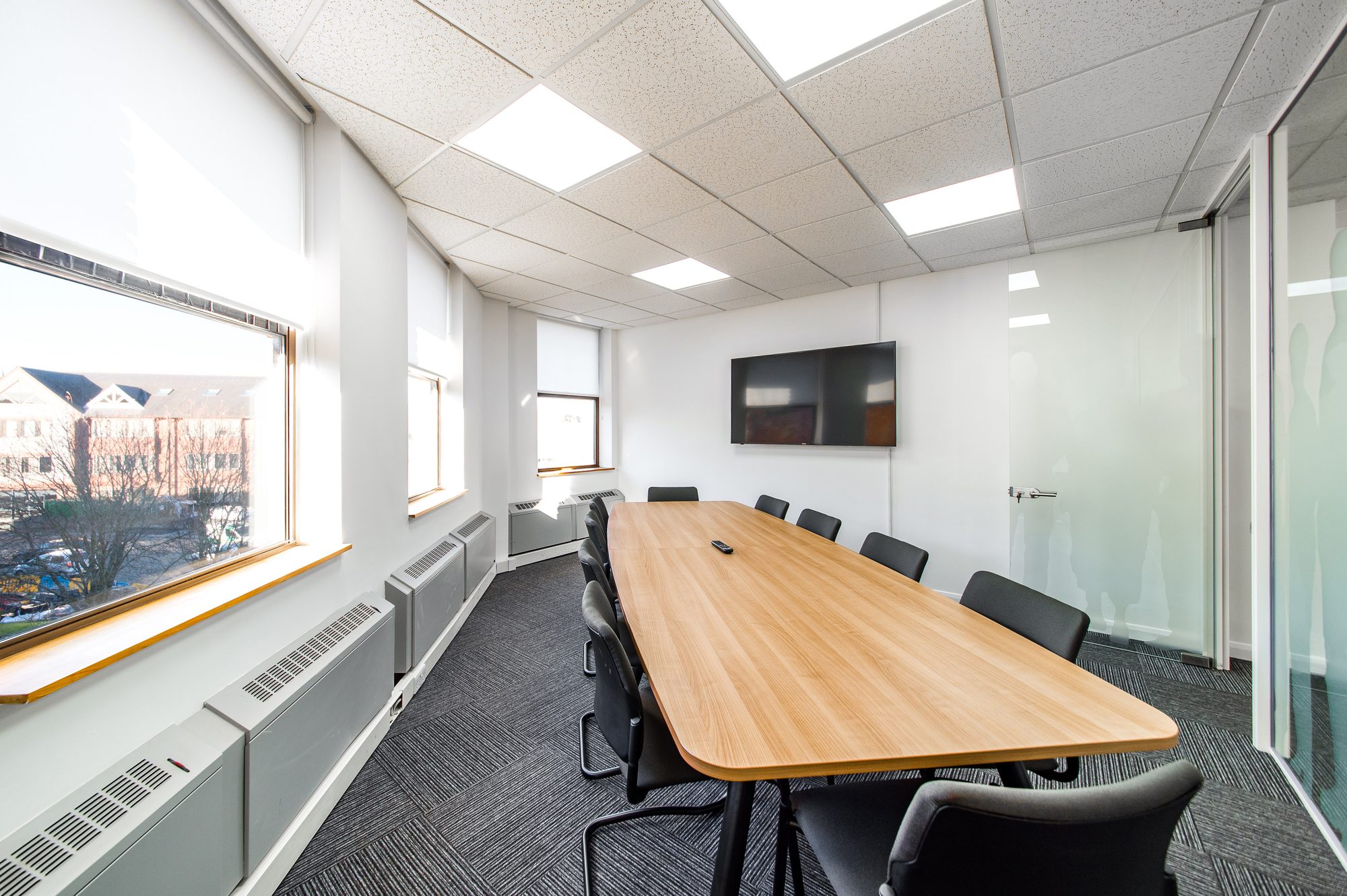 Boardroom with woodgrain table, leather chairs and dual TV screens