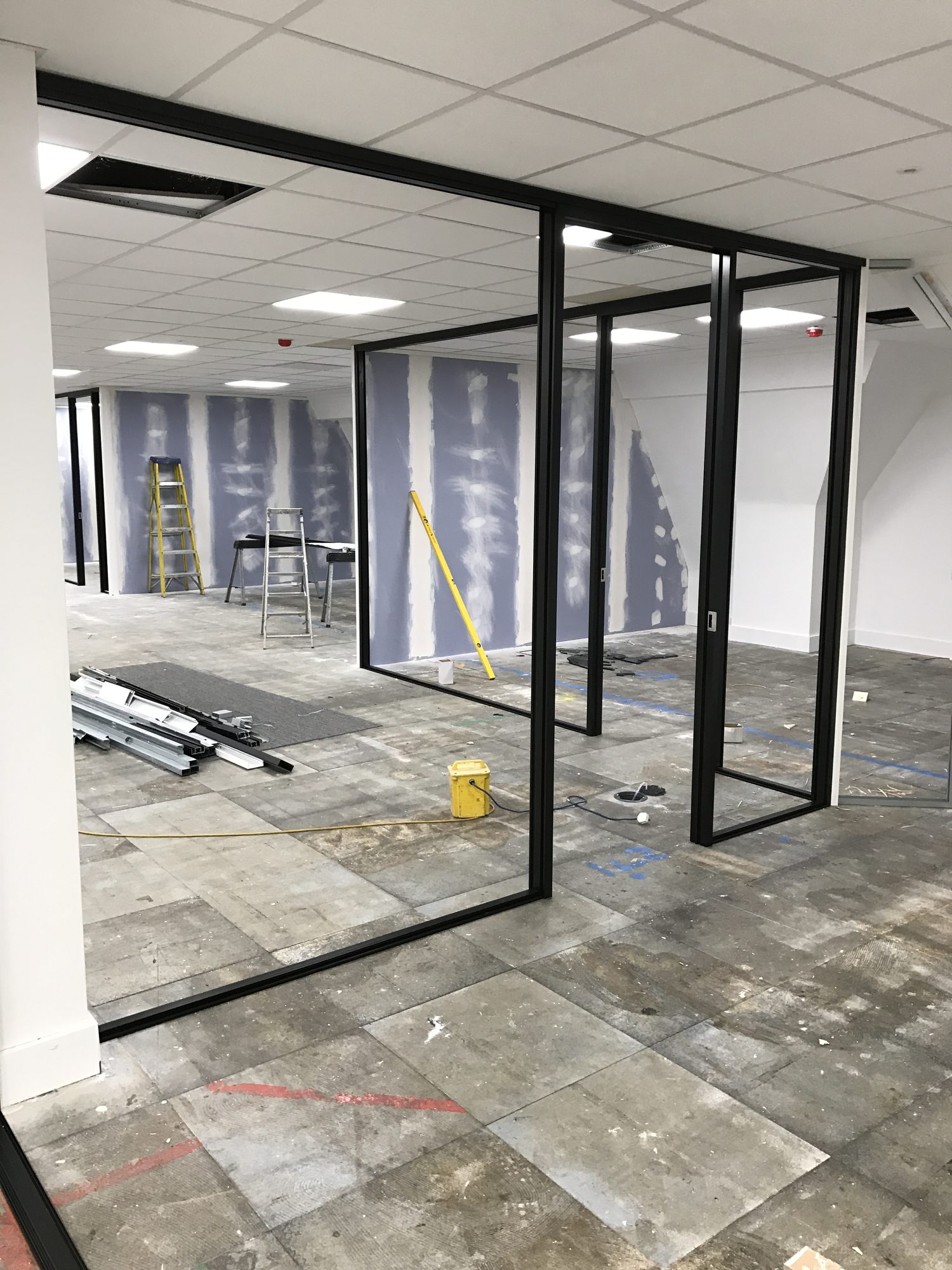 Black-framed glazed partitions installed, insulation visible behind plasterboard