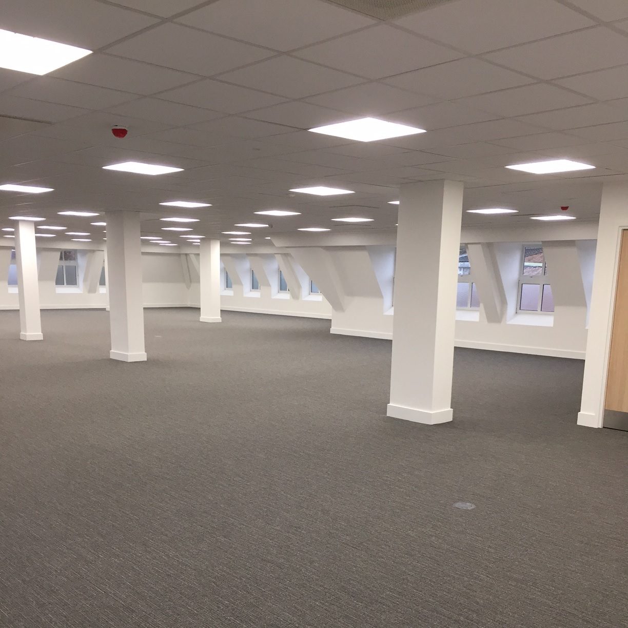 Empty second floor after Cat A fit-out, looking across white columns and fresh carpet