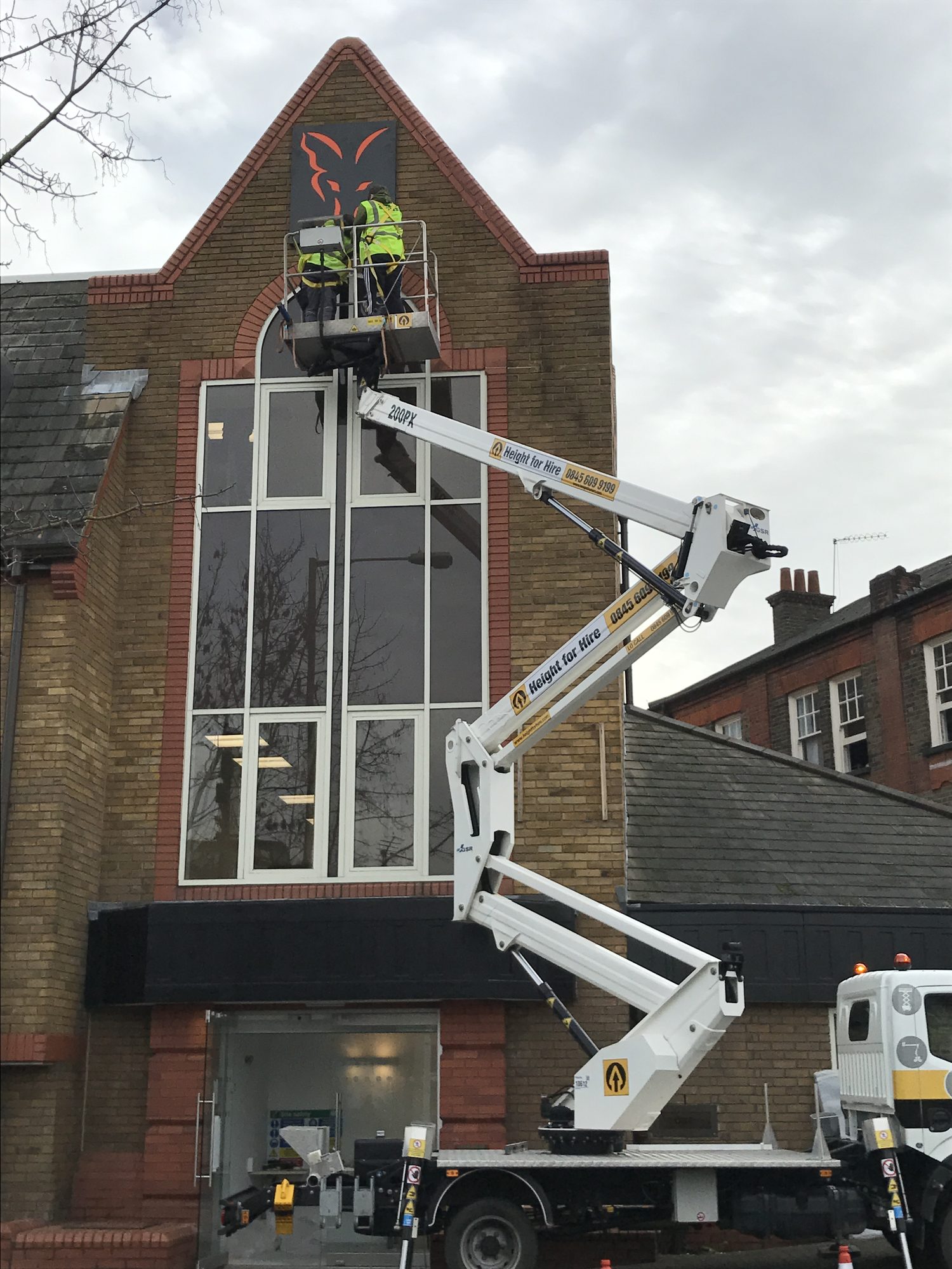 Installers fitting the Fox crest to the apex of the building from a cherry picker