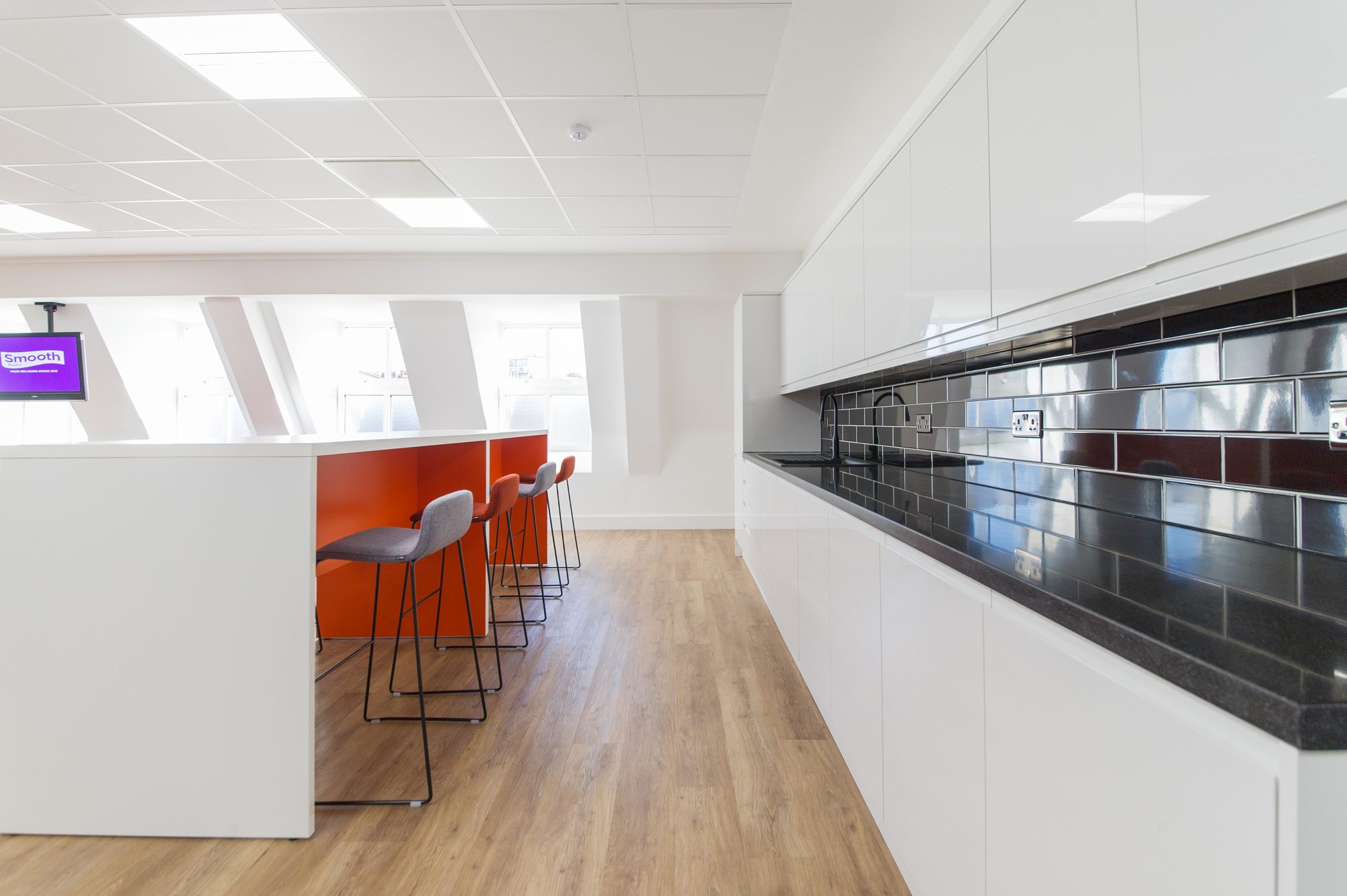 Kitchen with white units, black tile splashback and orange high counter