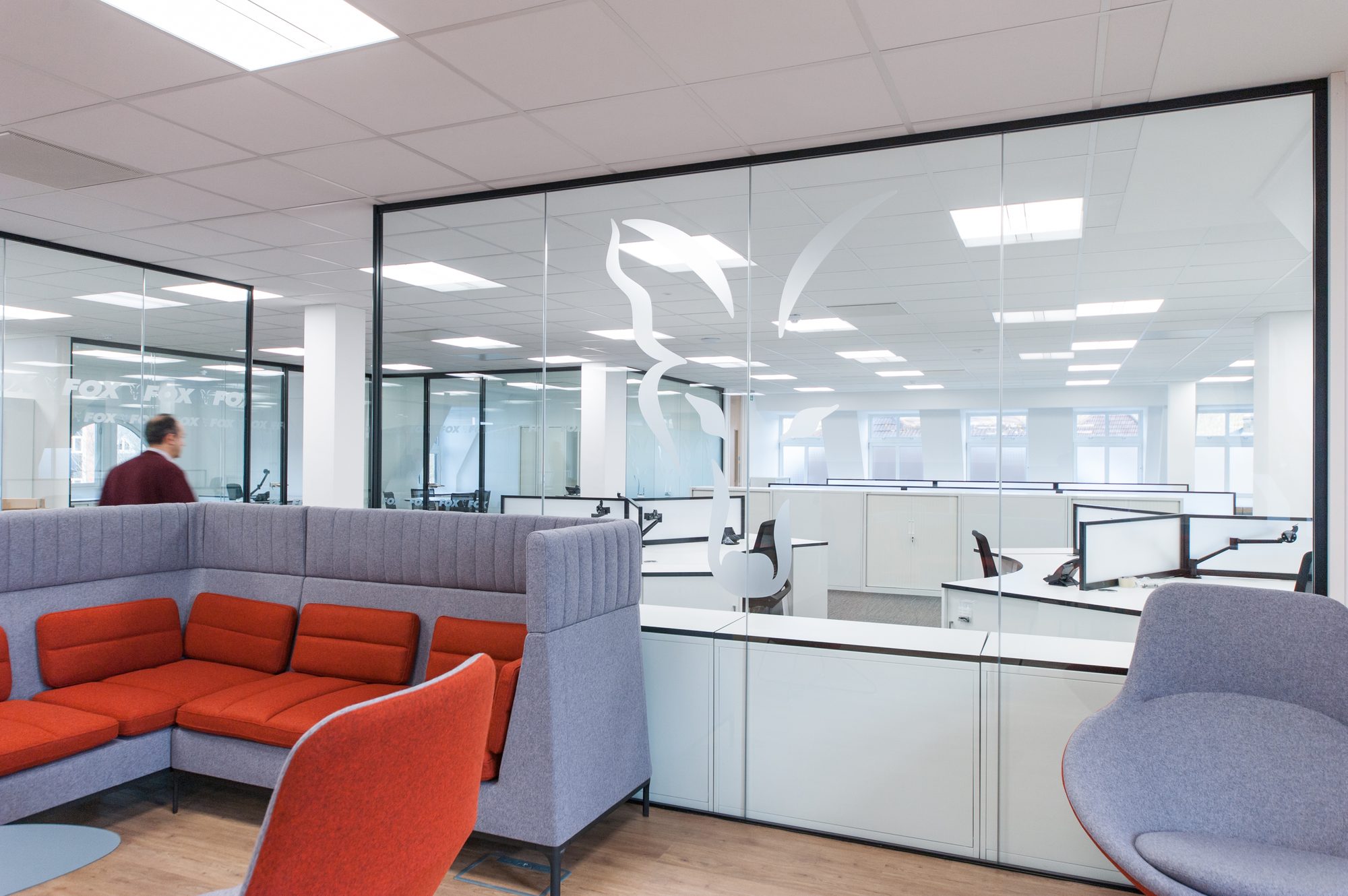 Open plan with orange and grey breakout snug, Fox logo manifested on glass partition, workstations beyond
