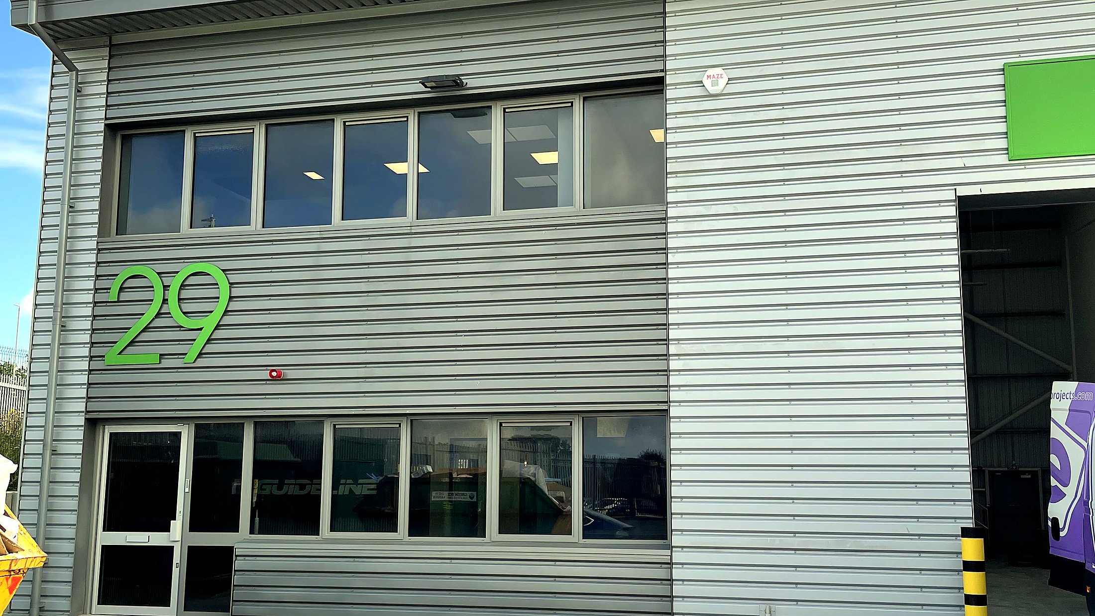 Guideline Lift Services HQ exterior. Grey cladding warehouse unit with green 29 signage, office windows above the entrance and Guideline branding on the door