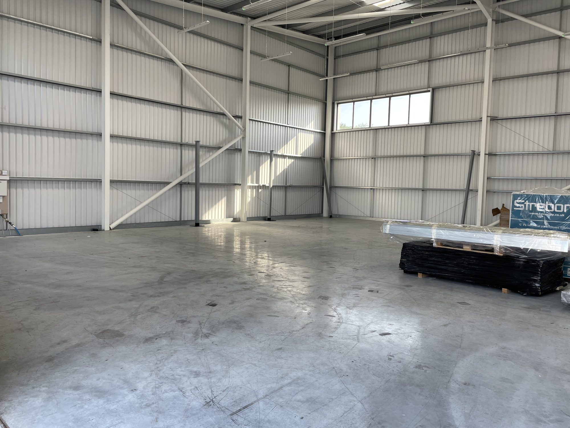 Empty newly built warehouse shell with bare floor slab, exposed steel portal frame and high level window