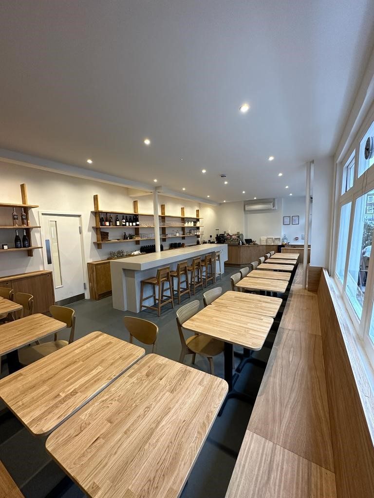Micro-cement bar with KURO wordmark debossed into the front, oak stools and oak shelving behind