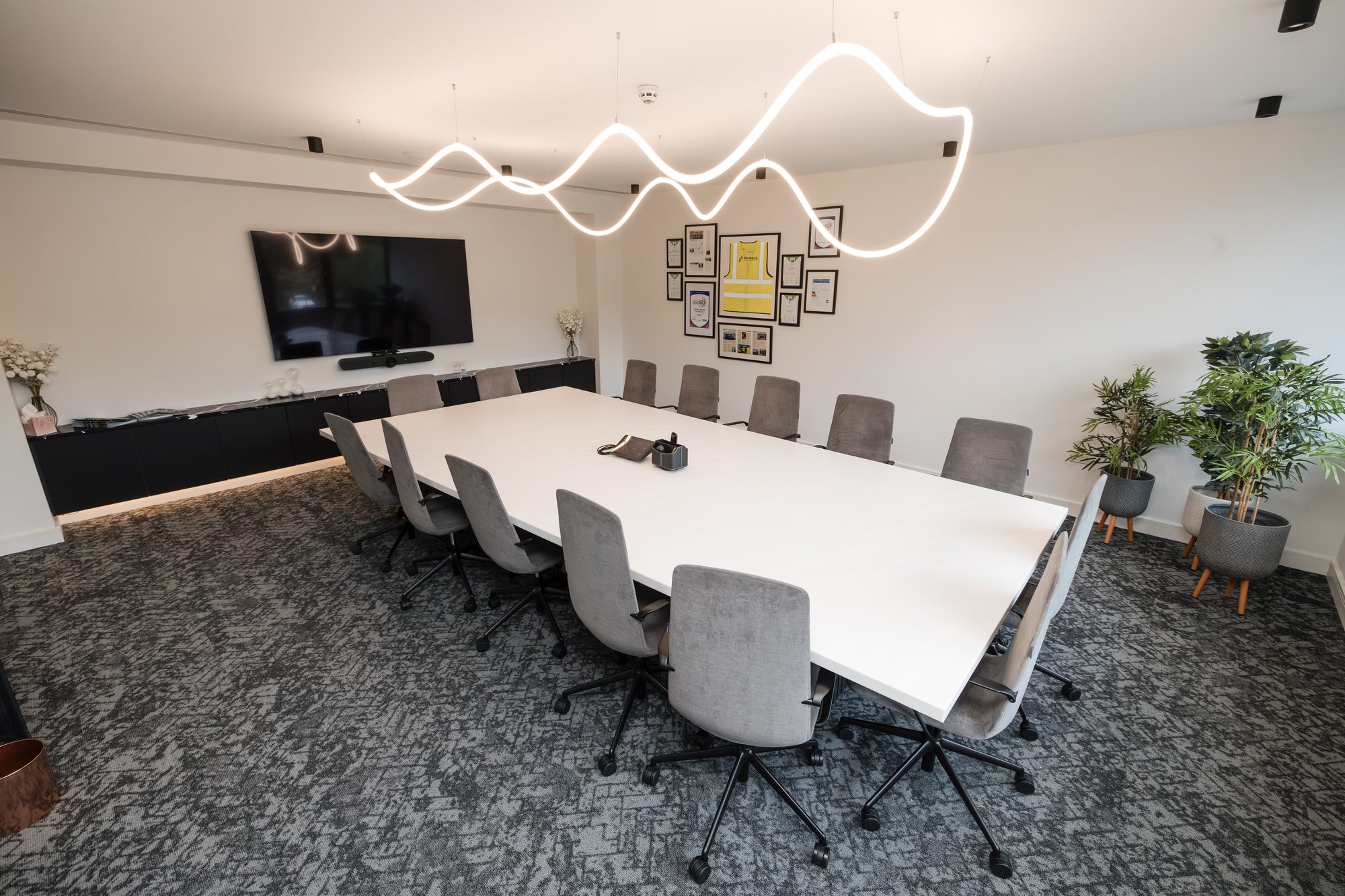 Boardroom with white table, grey velvet chairs, plants and sculptural wavy LED light feature overhead