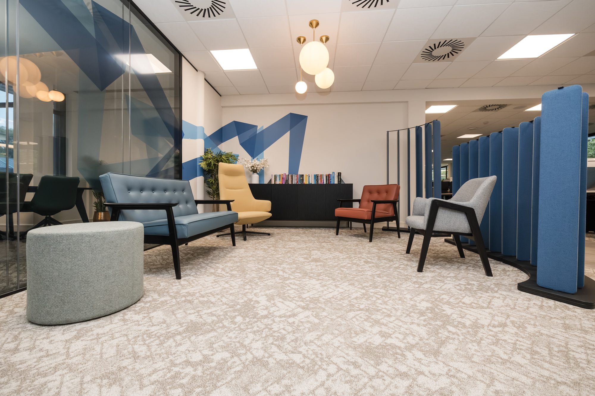 Breakout area with blue feature wall, mustard yellow, terracotta and grey armchairs and acoustic baffle dividers