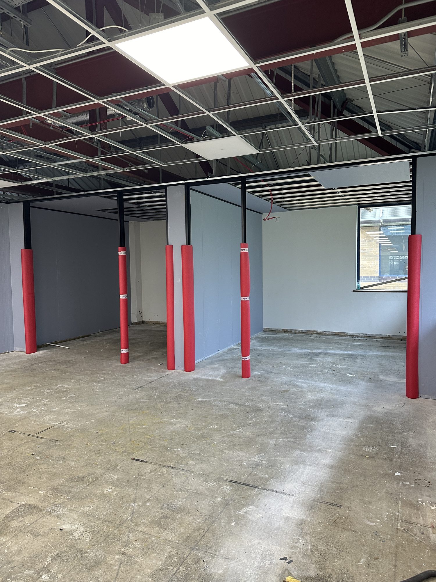 Suspended ceiling installation in progress with red column protectors still in place