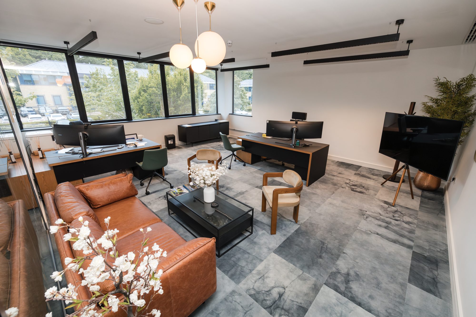 Executive office with brown leather sofa, dual monitor workstations, pendant lights and marble-tile floor