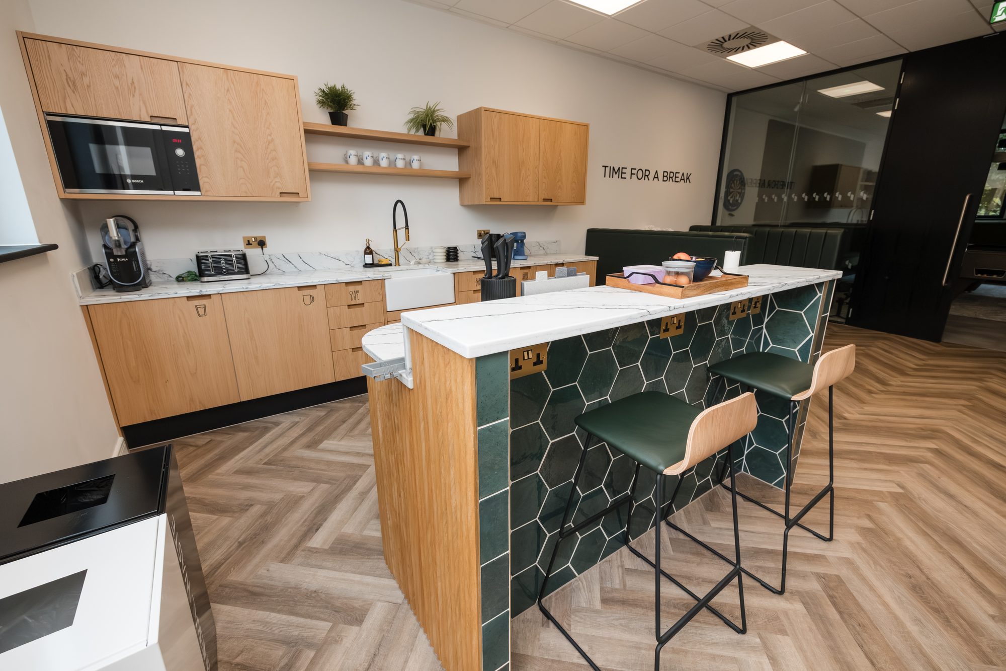 Bespoke kitchen with solid oak doors, green hexagonal tile feature wall and TIME FOR A BREAK signage on a marble counter island